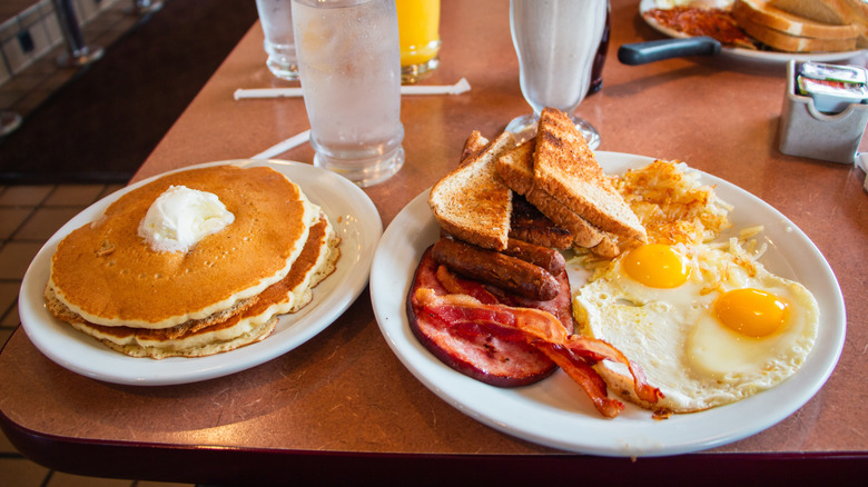 A breakfast diner table with plates of breakfast food like pancakes and eggs.