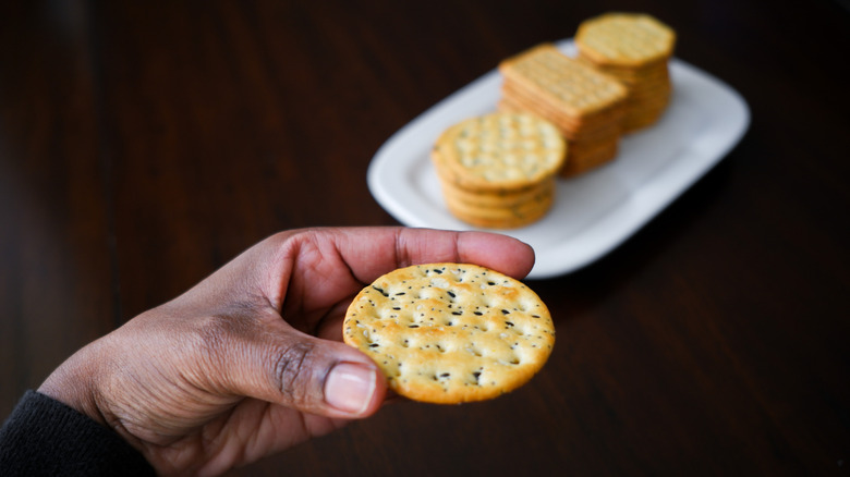Woman holding a cracker with crackers on a plate in the background