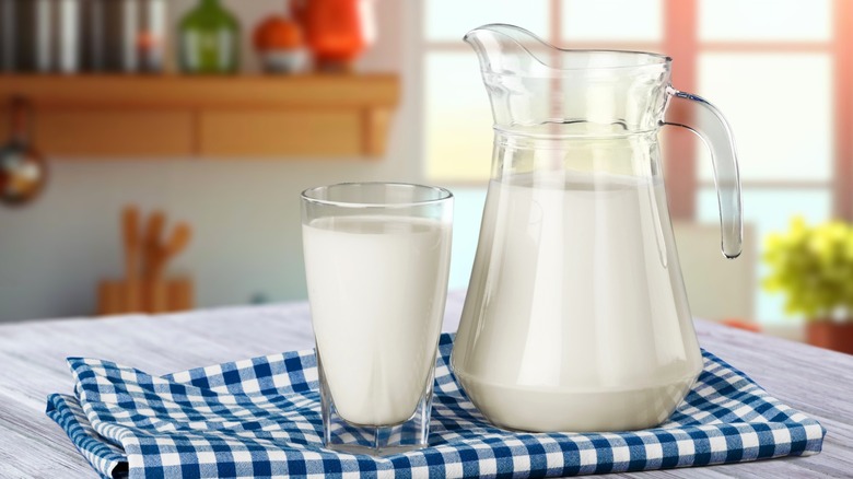 Glass pitcher and glass filled with milk on blue and white checkered tablecloth