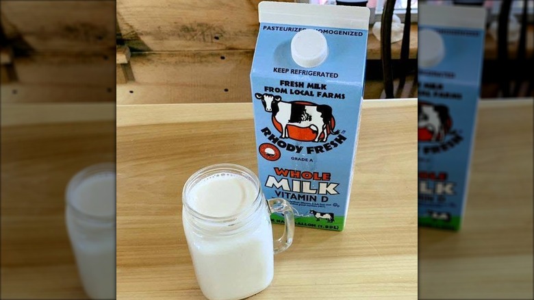 Carton of Rhody Fresh Milk next to filled glass on wood table