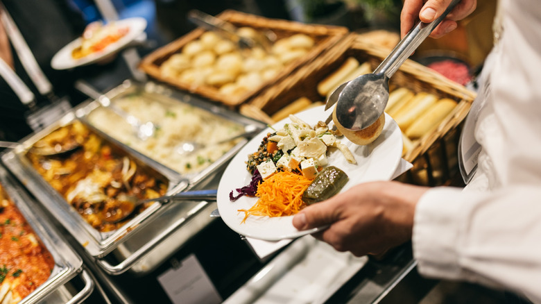 person filling their plate with various foods at a buffet