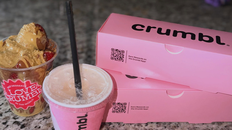 Two boxes of Crumbl cookies stacked next to a drink and Chocolate Strawberry Cup
