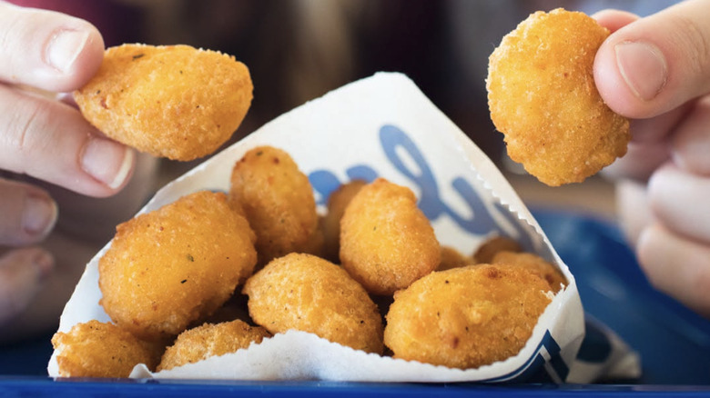 Hands holding cheese curds next to Culver's cheese curds in paper sleeve