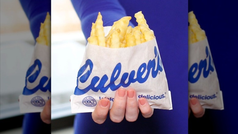 A Culver's employee holding an order of its crinkle cut fries