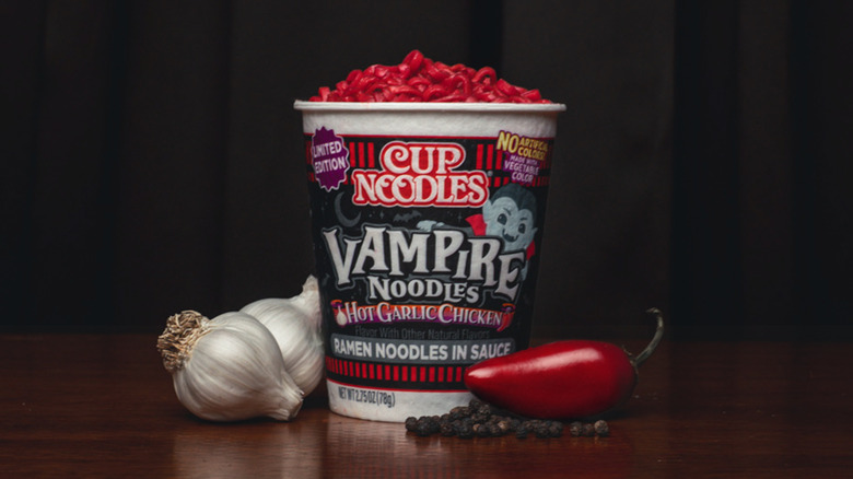 Cup Noodles Hot Garlic Chicken Vampire Noodles prepared in the cup alongside heads of garlic, black peppercorns, and a red chile pepper