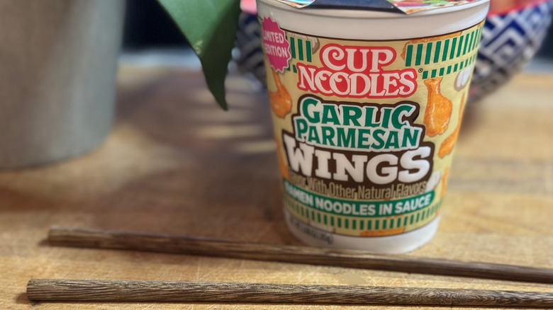 Cup Noodles Garlic Parmesan Wings flavor on wooden board with chopsticks by bowl and potted plant