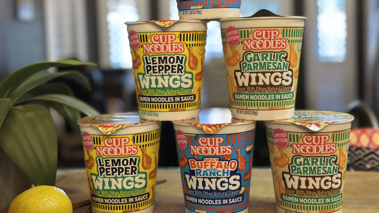New Cup Noodles Wings flavors stacked in pyramid on table next to lemon, potted plant, and chopsticks in living room