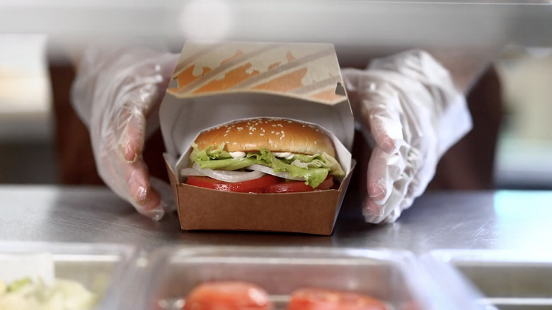 An image of the gloved hands of a fast food worker preparing a New Whopper.