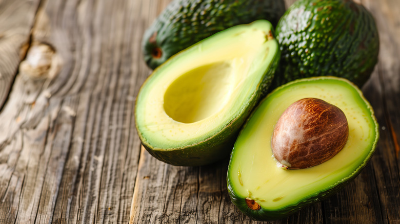 One cut avocado and two whole avocados in background.