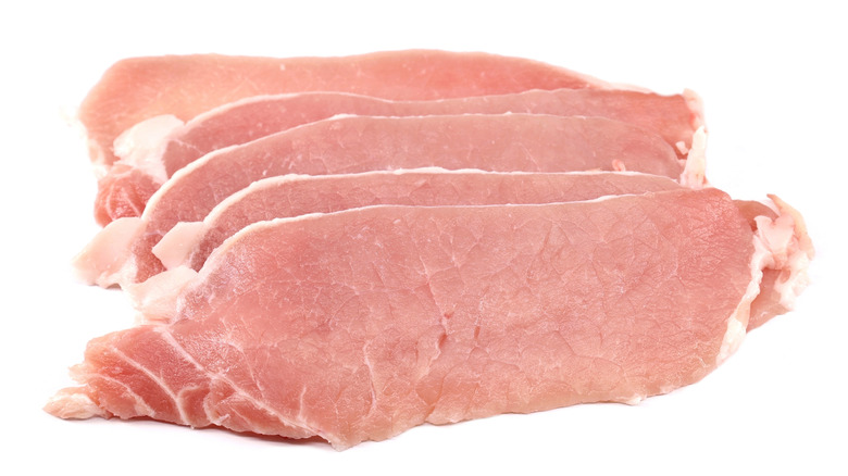 Uncooked thin pork loin steaks on white background.