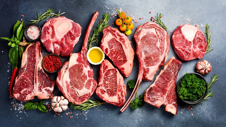 Various cuts of raw steak surrounded by spices and herbs