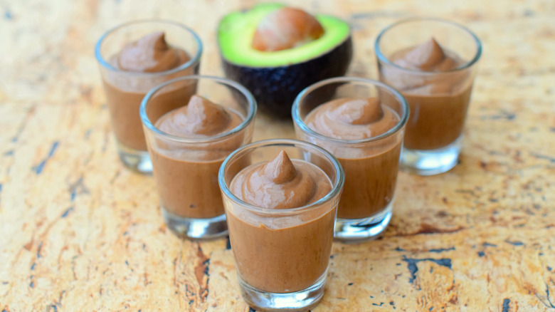 small cups of chocolate avocado mousse with a half sliced avocado in background