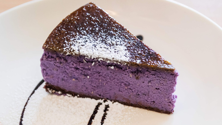 Slice of purple sweet potato cheesecake on plate dusted with powdered sugar