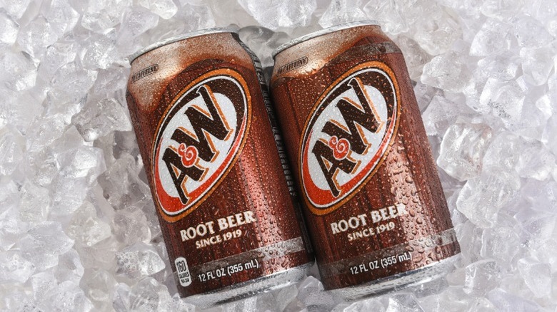 Two cans of A&W root beer laying on a bed of ice.
