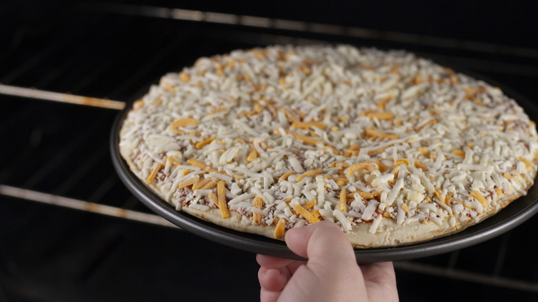 Frozen cheese pizza being loaded into home oven.