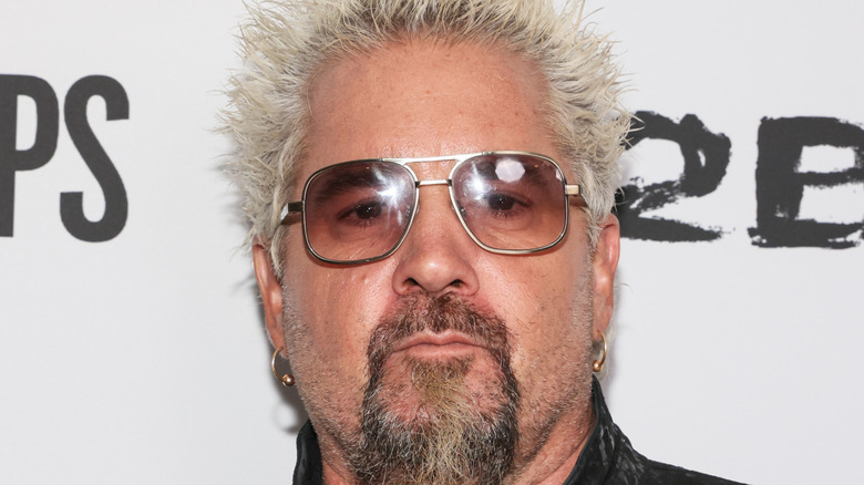 Closeup of Guy Fieri posing on red carpet for event.