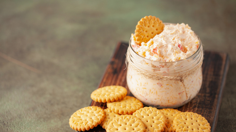 Pimento cheese dip in jar with crackers on wooden board