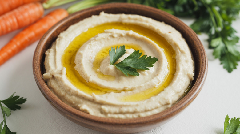 Wooden bowl of hummus with drizzle of olive oil and parsley leaf