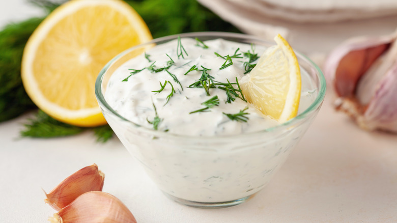 Sour cream dip in clear bowl with herbs, lemon wedge, and clove of garlic