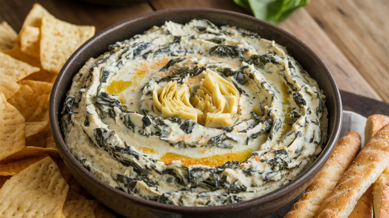 Bowl of spinach and artichoke dip surrounded by artisan crackers