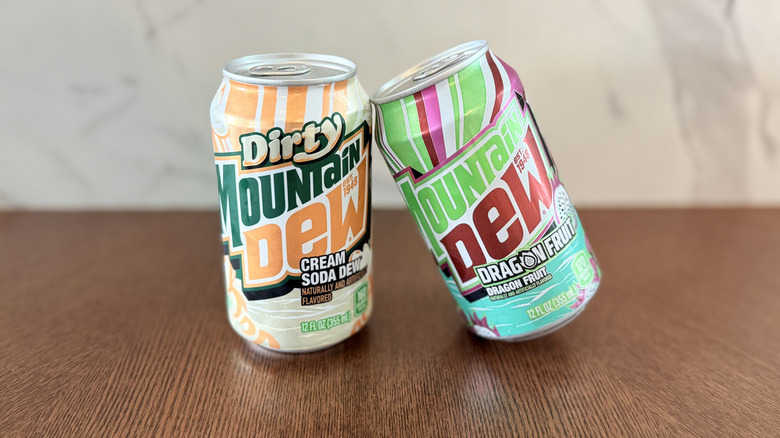 One can of mountain dew dragon fruit leaning against another can of mountain dew dirty cream soda