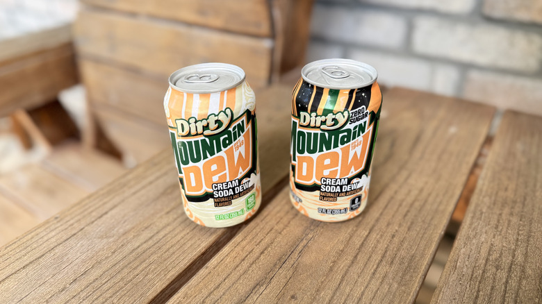 Two soda cans of mountain dew dirty cream soda on wooden chair