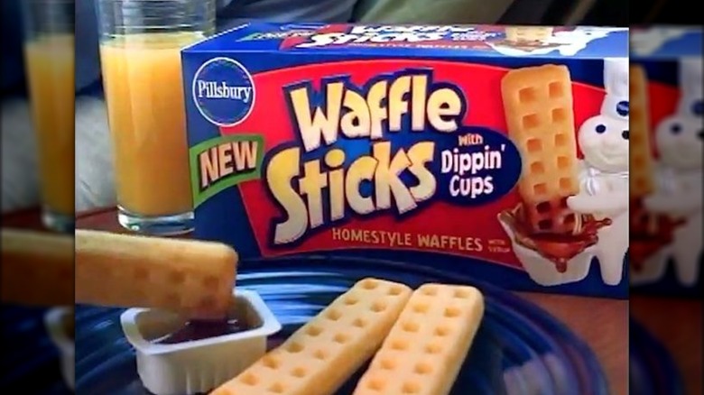A box of Pillsbury Waffle Sticks with Dippin' Cups on a table with a glass of orange juice and some waffle sticks on a plate.