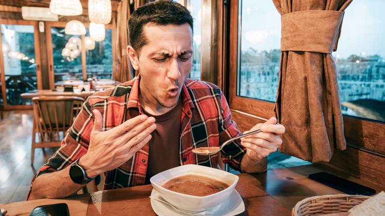 A man fanning his mouth after eating spicy soup in a restaurant
