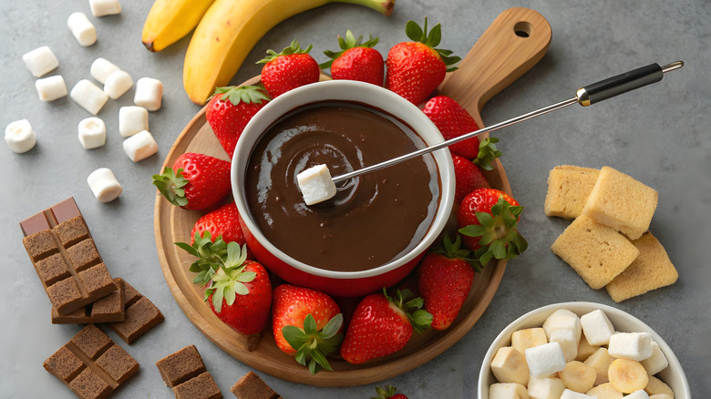 Chocolate fondue surrounded by strawberries, marshmallows, and chocolate
