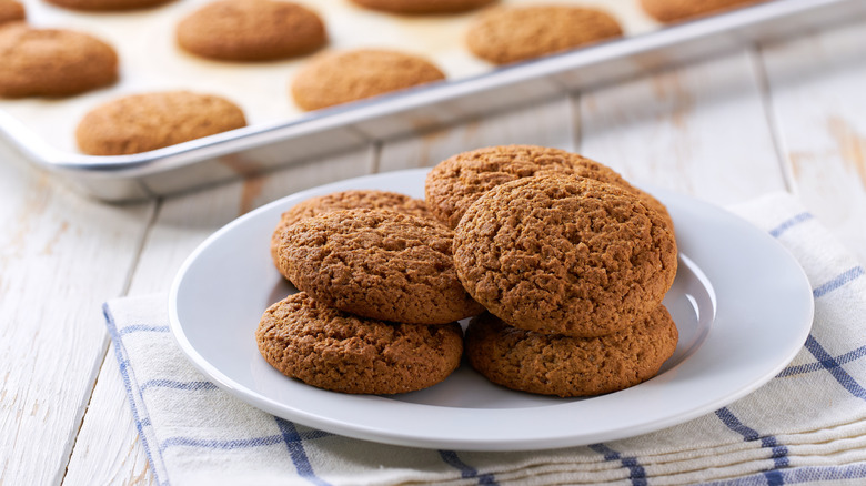 Freshly baked oatmeal cookies on white plate with baking tray in backdrop