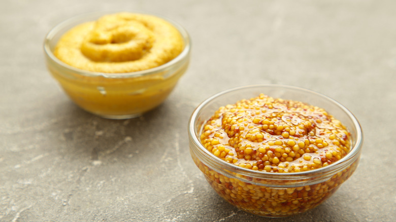 Two small glass bowls of different kinds of mustard.