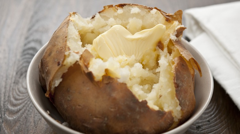 baked potato split open in a bowl with a pat of butter inside it