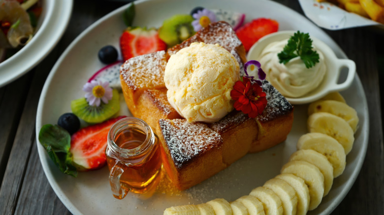 French toast topped with vanilla ice cream, along with fruit, butter, edible flowers, and honey