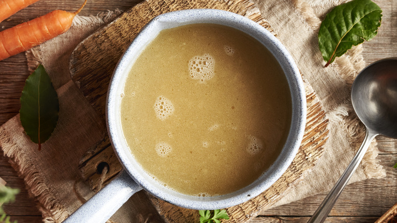 Chicken broth in a pan surrounded by vegetables and herbs