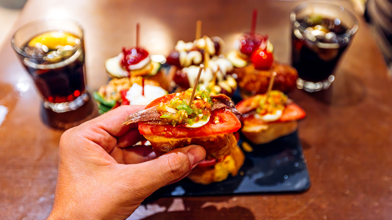 Hand holding bread topped with colorful ingredients skewered with toothpick