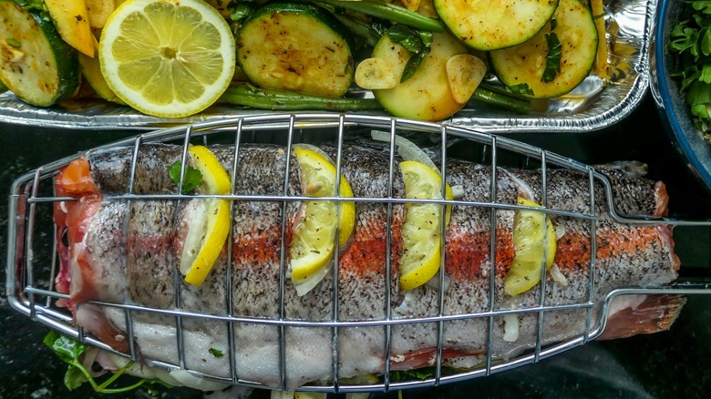 Raw fish in grill basket with lemon wedges and veggies in a side dish