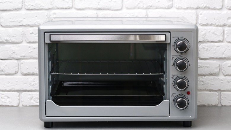 A modern countertop toaster oven sitting on the counter against a white brick wall.