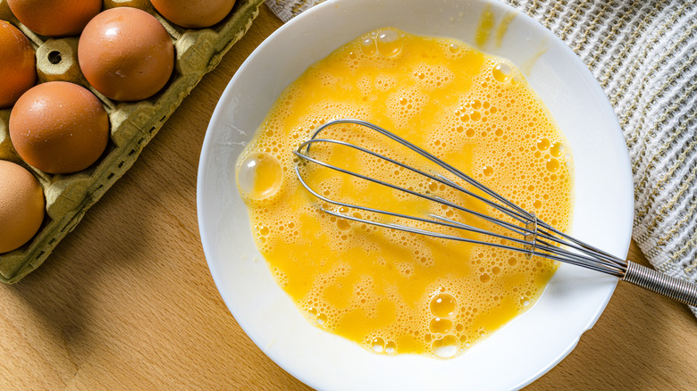 Whisked eggs in a bowl with a carton of brown eggs