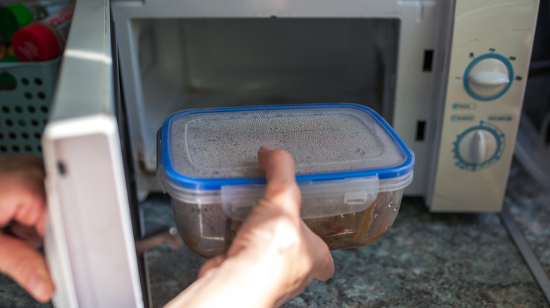 A hand putting a Tupperware container into an open microwave