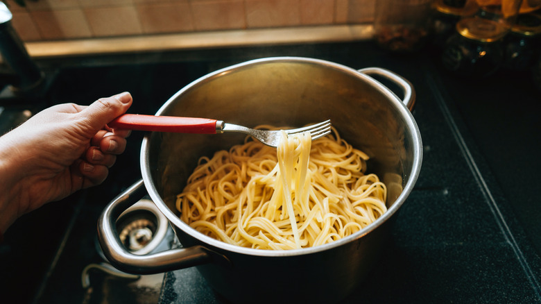 a hand holding a fork with pasta noodles on its tines