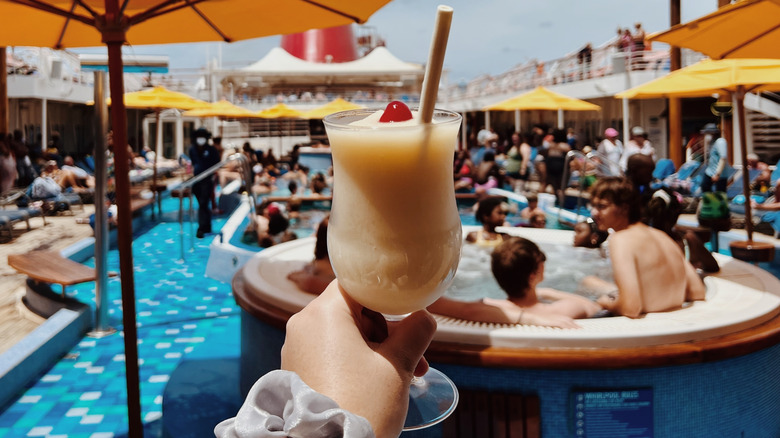 Holding a pina colada in front of a crowded pool