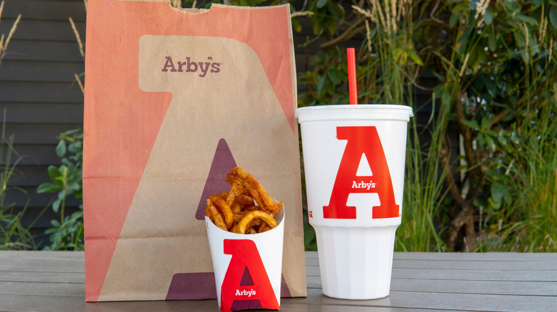 A bag of Arby's food including curly fries and a drink