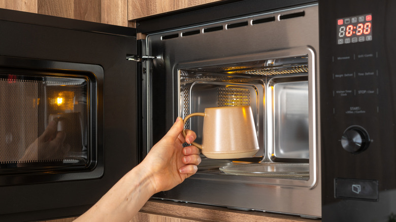 Hand putting a coffee mug in the microwave