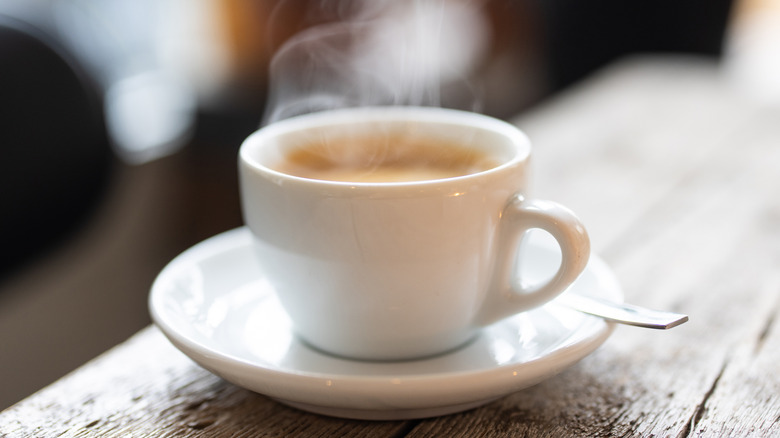 A white cup of coffee on a saucer with steam rising from it