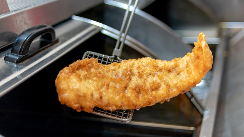 Person lifting deep-fried fish from fryer with spatula