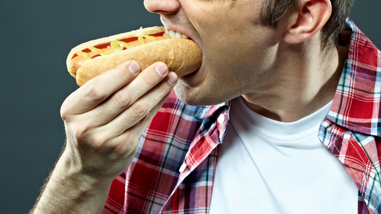 A man in a plaid shirt eating a hot dog