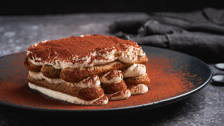 Tiramisu served on a black plate.