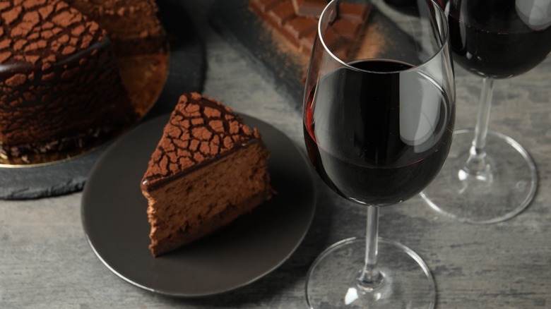 A glass of red wine sitting next to a plate of chocolate cake