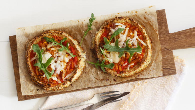 Two cauliflower crust pizzas on wooden board