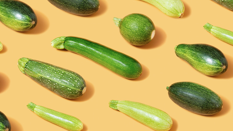 Various sizes and shapes of zucchini on an orange background